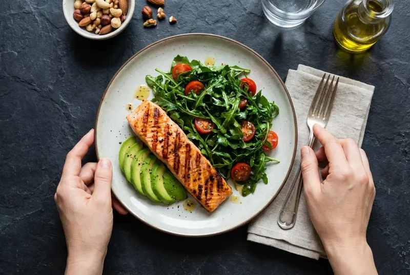 Overhead view of a healthy plate with salmon, avocado, and greens on a rustic table.