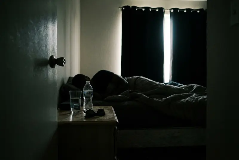 A silhouette of a person resting in a dark room with electrolytes on the nightstand.