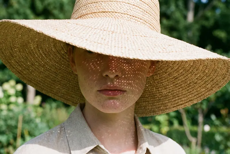 Close-up of a wide-brimmed straw hat casting a shadow over a woman's face.